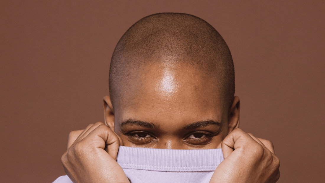 African American woman with bald head covering her face